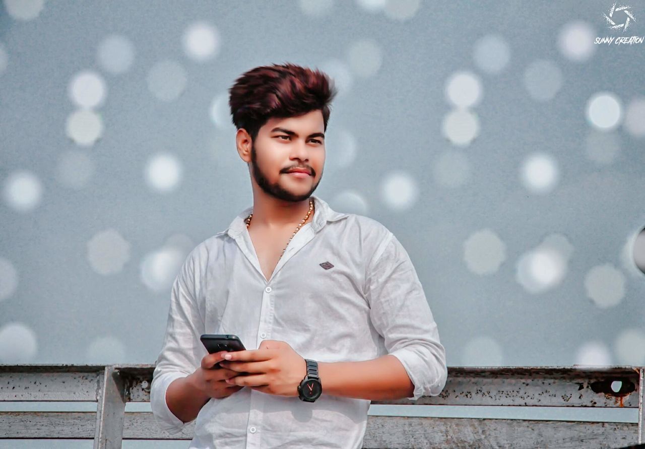one person, young adult, front view, portrait, wireless technology, mobile phone, smiling, looking at camera, casual clothing, real people, leisure activity, holding, waist up, happiness, lifestyles, technology, looking, young men, smart phone