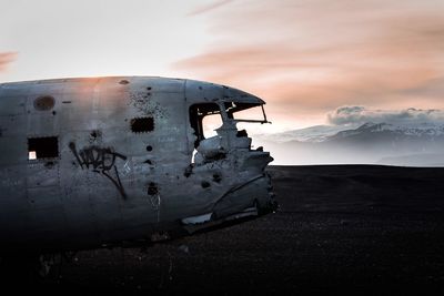 Abandoned airplane on landscape against sky during sunset