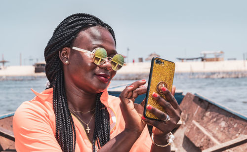 African woman sitting on a boat with mobile phone in hand and taking photos