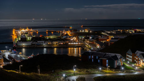 High angle view of illuminated city by sea against sky at night