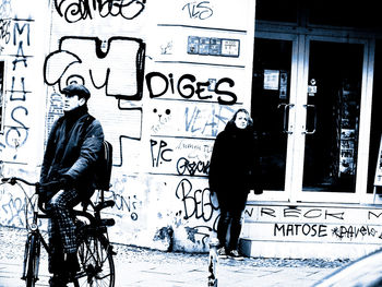 People standing by graffiti on wall