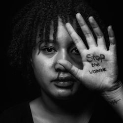 Portrait of teenage girl covering face against black background