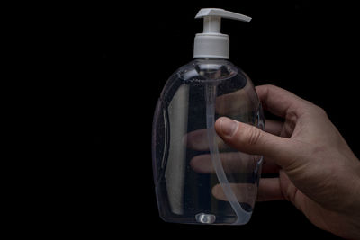 Close-up of hand holding bottle against black background