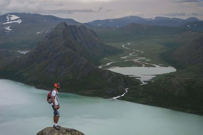 Full length of man standing on rock by lake and mountains at jotunheimen