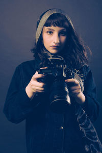 Portrait of young woman standing against black background