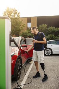 Man with prosthetic leg charging electric car at station