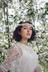 Portrait of a young beautiful woman in white clothes standing next to blooming cherry tree in spring