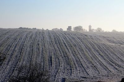 Snow covered field against clear sky on sunny day