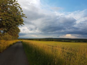 Road passing through field against cloudy sky