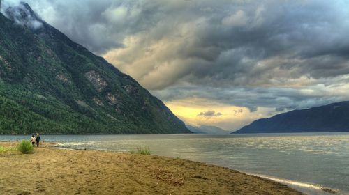 Scenic view of lakeside mountains against cloudy sky