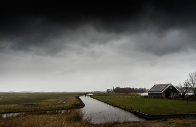 Scenic view of field by houses against sky