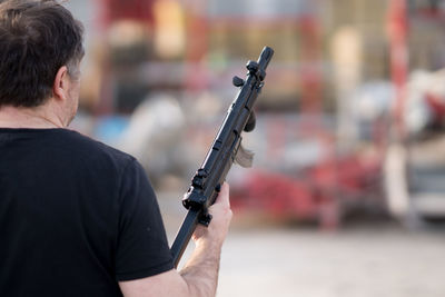 Rear view of man holding rifle on ground