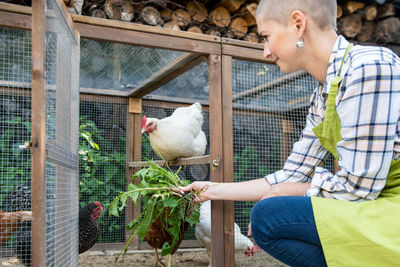 Smiling woman feeding hen in farm