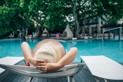 Woman relaxing on lounge chair by swimming pool at tourist resort