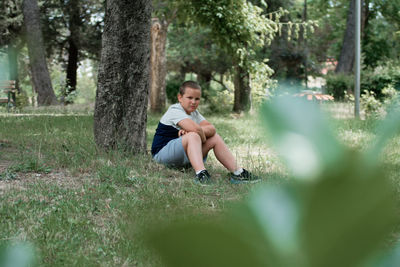 Full length portrait of boy sitting on tree