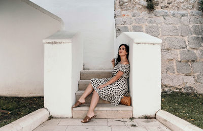 Beautiful young woman in polka dot dress sitting on stairs in old town.