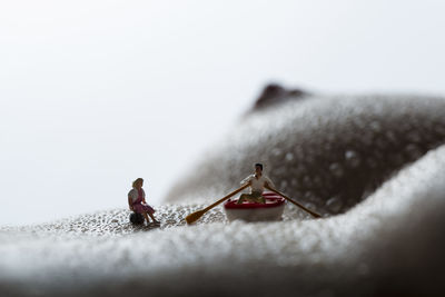 Close-up of figurines on wet shirtless woman against white background