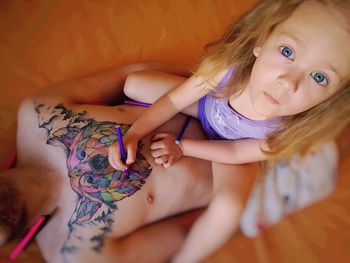 High angle portrait of cute daughter drawing on father chest at home