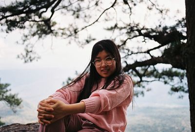 Portrait of young woman standing against trees