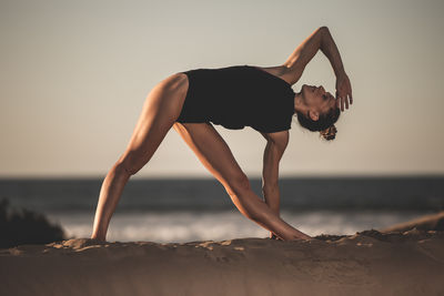 Woman exercising at beach against sky