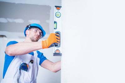 Worker using level on white wall