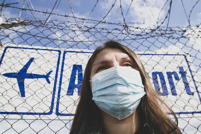 Low angle view of woman wearing mask standing against fence