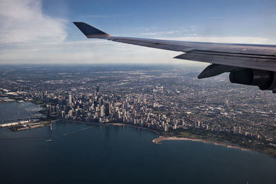 Cropped image of aircraft wing over city against sky