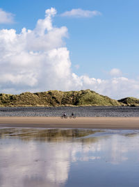 Distant view of people cycling at beach against sky