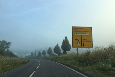 Information sign by empty road against sky during foggy weather