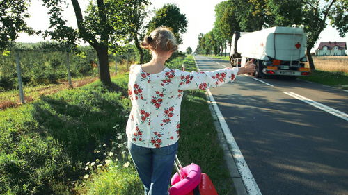 Woman with suitcase hitchhiking on roadside