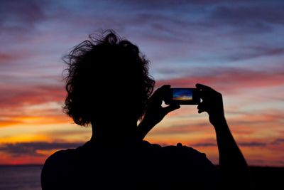 Rear view of silhouette person photographing against sky during sunset