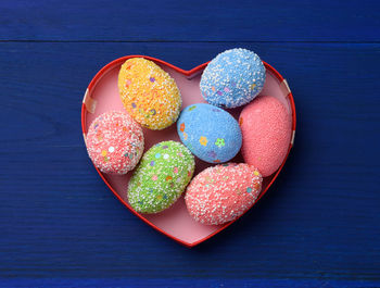 Decorative easter eggs in a cardboard box on a blue wooden background, top view