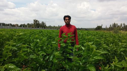 Portrait of mid adult man standing in farm against cloudy sky