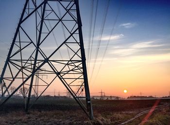 Electricity pylons on field at sunset