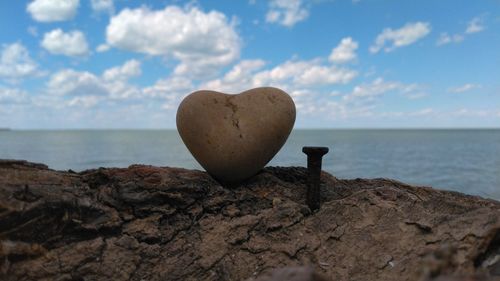 Heart shape on rock by sea against sky