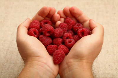 Cropped hand with fresh raspberry fruits over table