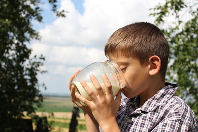 A boy in a checkered shirt enjoys fresh milk in the village in the summer