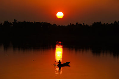 Silhouette man in boat on lake against sky during sunset