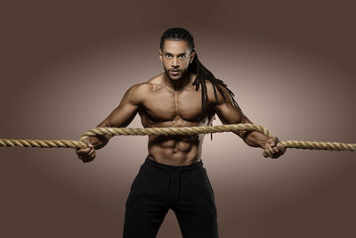 Portrait of athlete exercising with rope against brown background