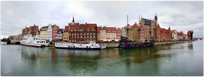 Panoramic view of boats on river by buildings in city against sky