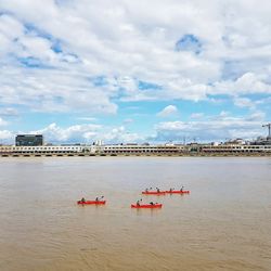 Mid distant view of people kayaking in river by city against sky