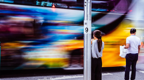 Rear view of man and woman standing by bus on road