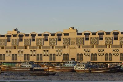 Boats in river by buildings against clear sky