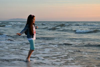 Girl wading in sea against sky during sunset