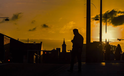 Silhouette man standing on street against orange sky