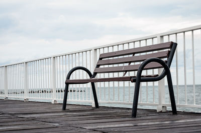 Empty chair on pier by sea against sky