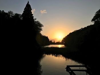 Silhouette trees by lake against sky during sunset