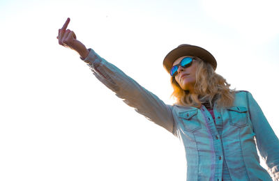 Woman in sunglasses showing obscene gesture against clear sky