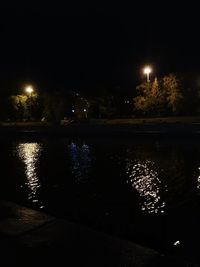 Illuminated city by river against sky at night