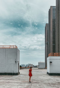 Rear view of woman standing by building against sky